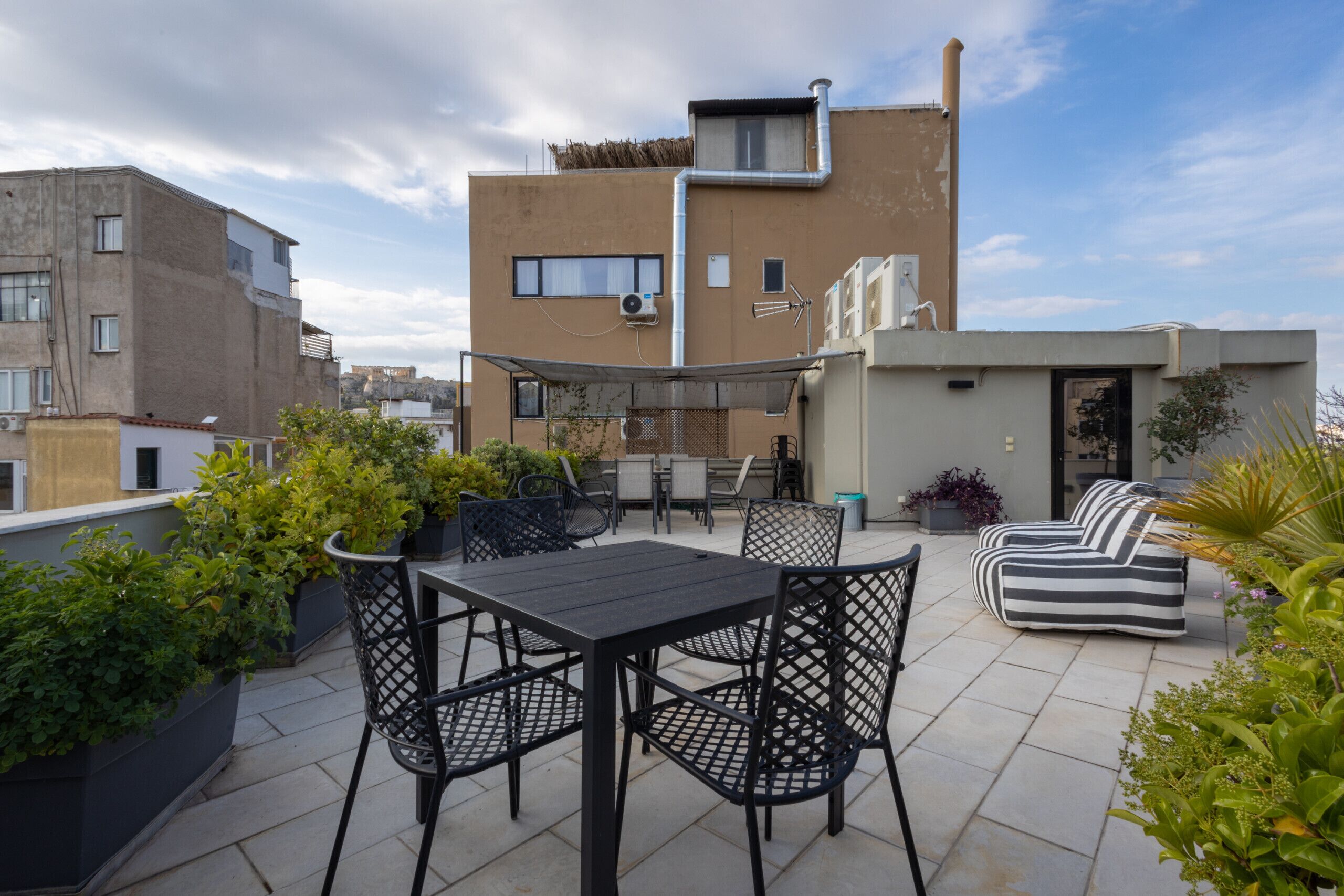 An outdoor patio with a table and chairs, a striped sofa, and potted plants.