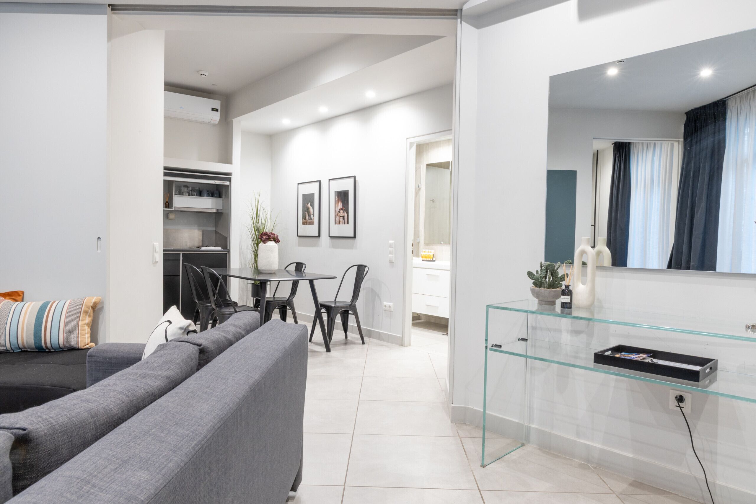Ein modernes Wohnzimmer mit grauem Sofa, einem Esstisch mit Stühlen und einer Küche im Hintergrund.