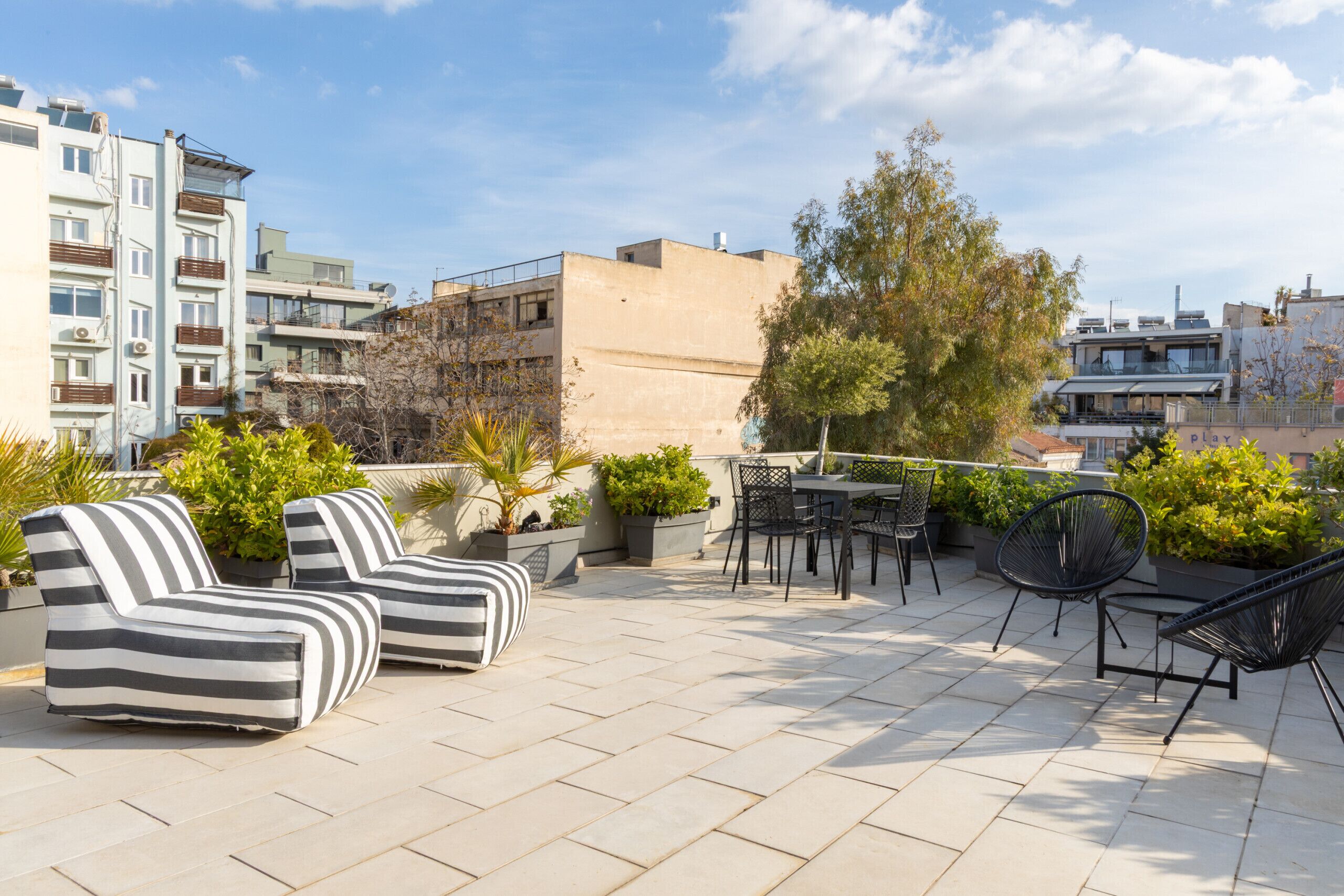 Une terrasse sur le toit, aménagée avec des espaces de détente en plein air, des plantes en pot et offrant une vue sur le paysage urbain.