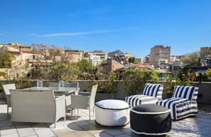 Ein Außenbereich mit einer Terrasse, Korbmöbeln, einem Glastisch und gestreiften Kissen.