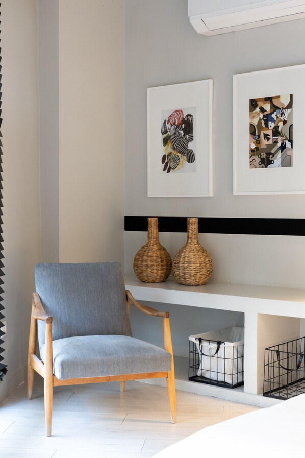 A modern living room with a grey armchair, two wicker vases on a shelf, and a framed abstract painting above. - Fantastic Central Athens Suite with Rooftop Deck (Athens)