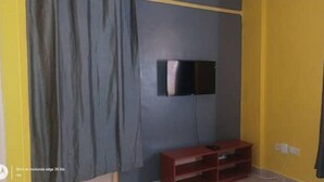 Une pièce avec un téléviseur à écran plat fixé à un mur foncé, un meuble de rangement rouge en dessous et un mur d’accent jaune.