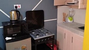 Une cuisine compacte équipée d’une cuisinière à gaz, d’un four à micro-ondes et d’une bouilloire. On y trouve également un petit réfrigérateur, un évier et un placard contenant de l’ustensile de cuisine.