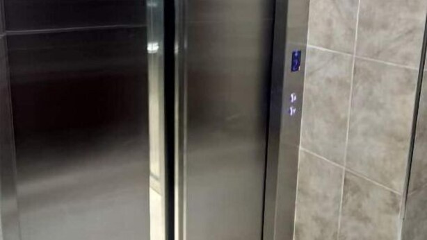 Une porte d’ascenseur en métal, dotée d’un panneau de commande et bordée d’un mur carrelé.