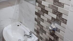Une salle de bain avec un lavabo blanc, un miroir et un mur recouvert de carreaux imitant un motif de briques.