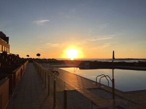 Eine Uferpromenade mit einem spiegelnden Teich, wolkenlosem Himmel und Sonnenuntergang.