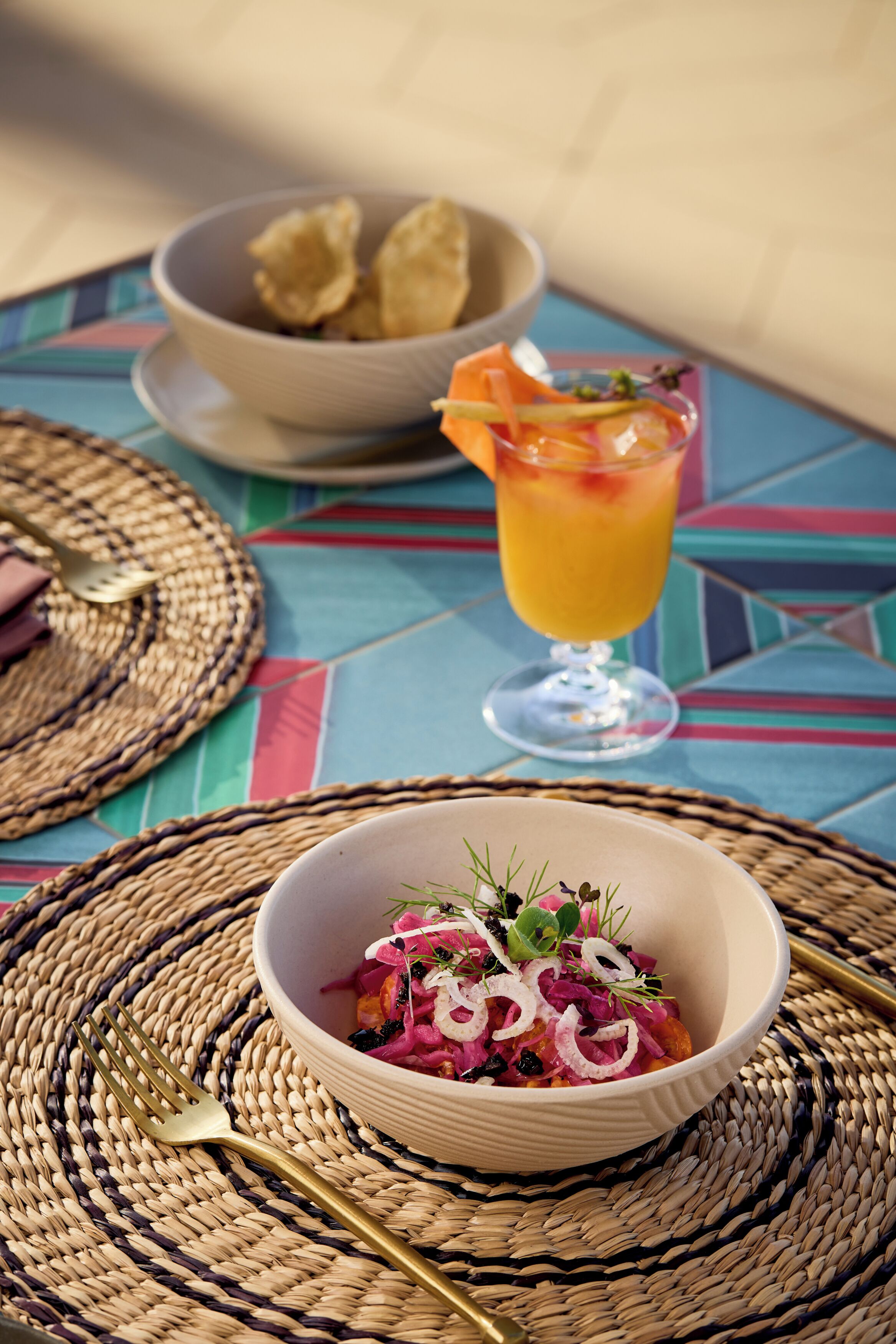 Una mesa dispuesta con un tazón de ensalada, un vaso de jugo de naranja y un plato de papas fritas.