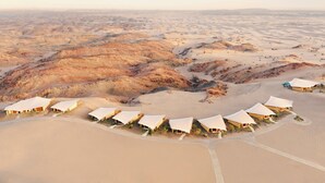 Un paysage désertique avec plusieurs tentes disposées en demi-cercle, entourées de dunes de sable et d’un terrain rocailleux.