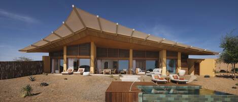 A modern house with a large covered patio, outdoor seating, and a swimming pool.
