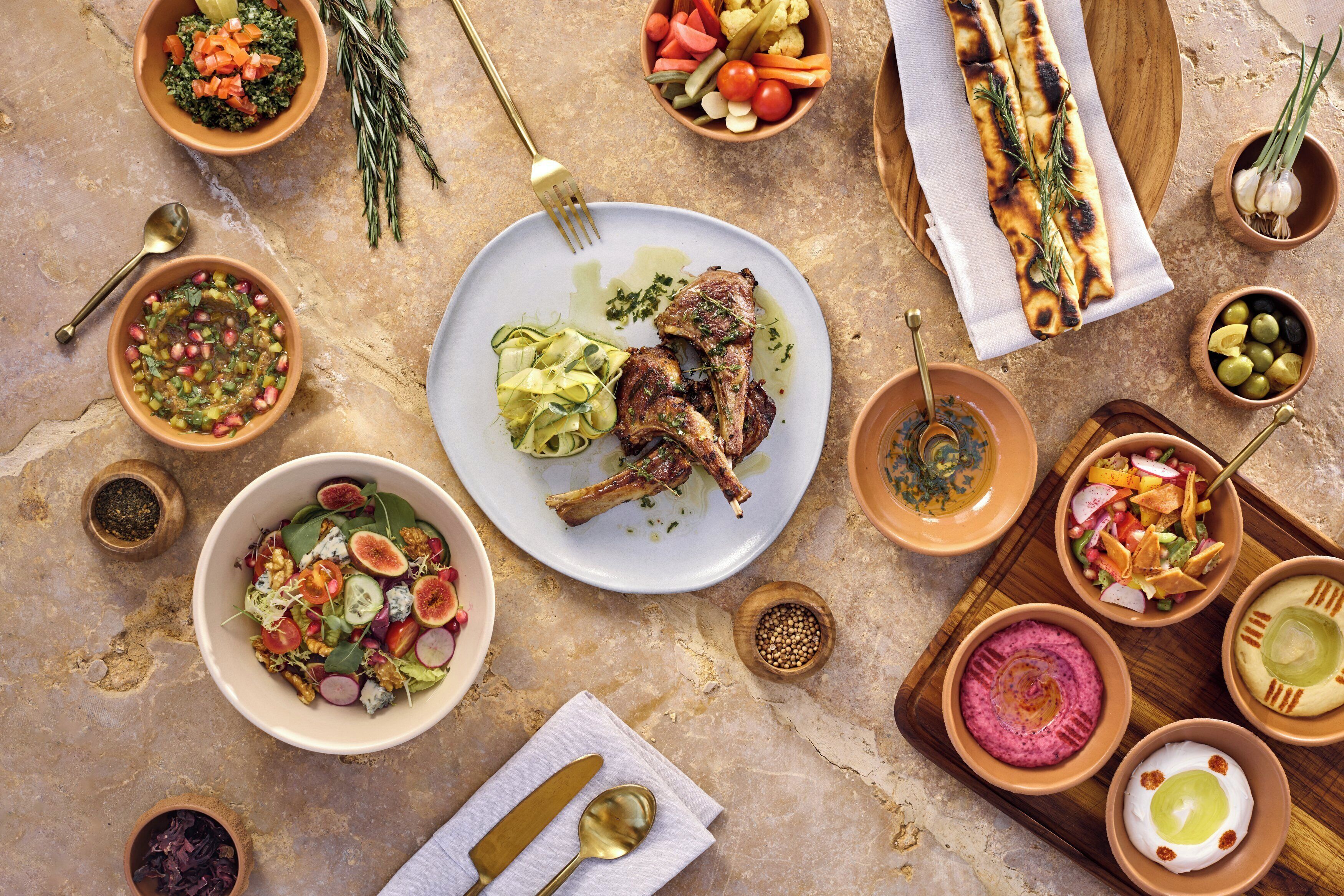 Une table dressée avec différents plats, notamment de la viande grillée, des salades et du pain, ce qui laisse supposer qu’un repas va être servi.