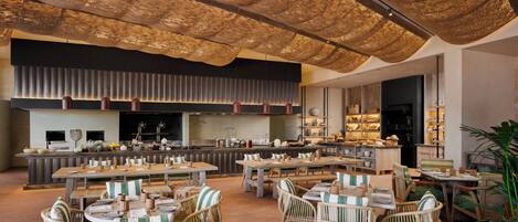 Een ruim restaurant met hoge plafonds, rieten meubels en een moderne keuken op de achtergrond.