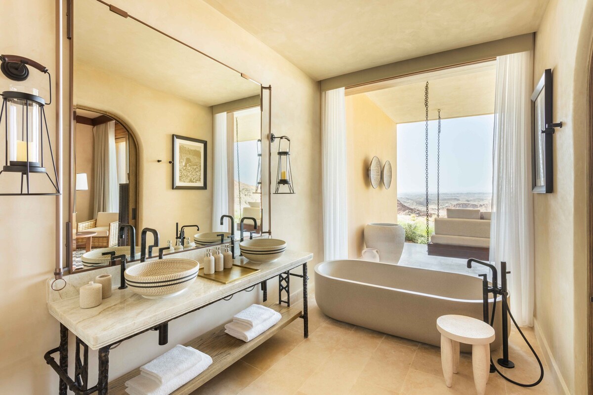 A modern bathroom with a freestanding bathtub, a large mirror, and a view of the landscape.