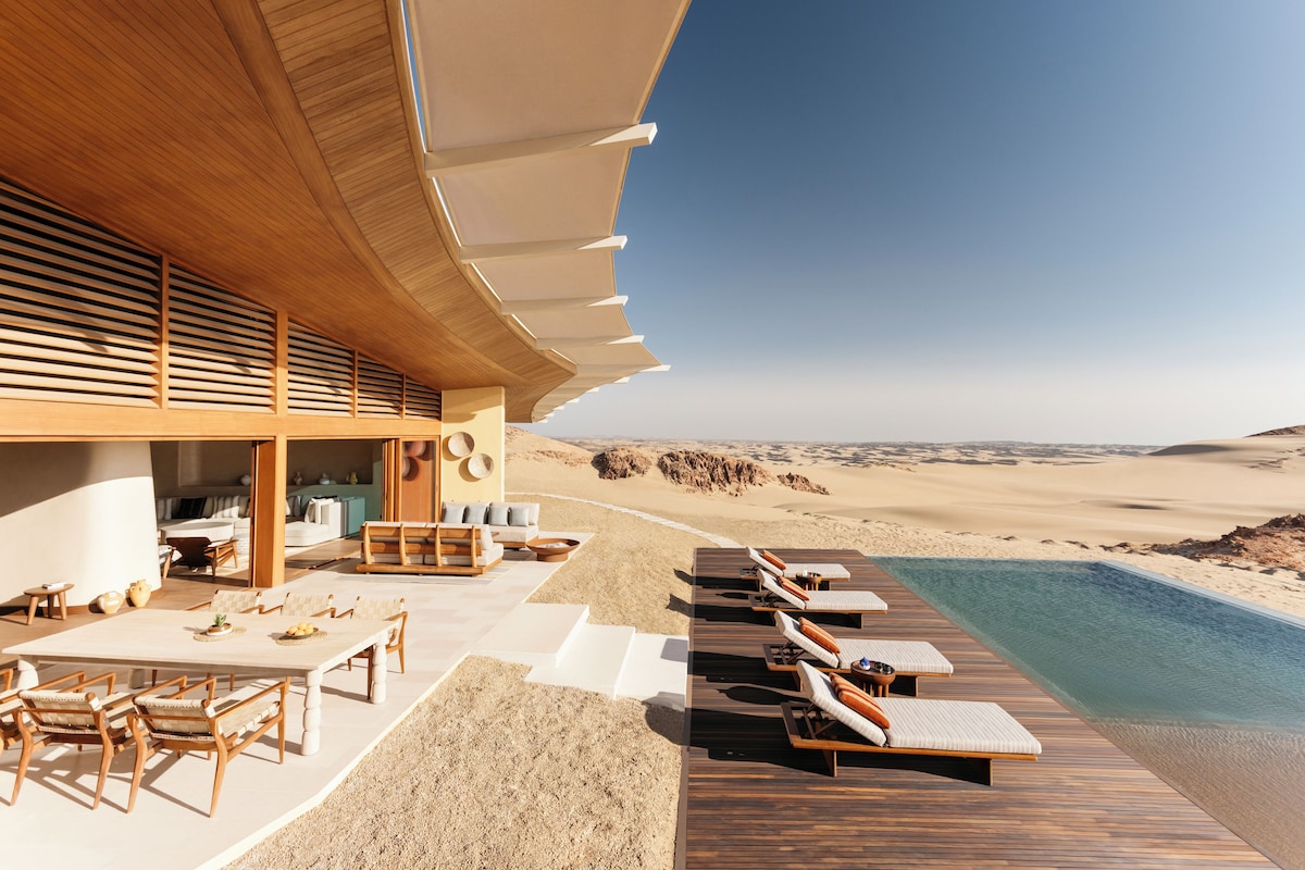 A modern resort with a pool, wooden deck, and lounge chairs overlooking a desert landscape.