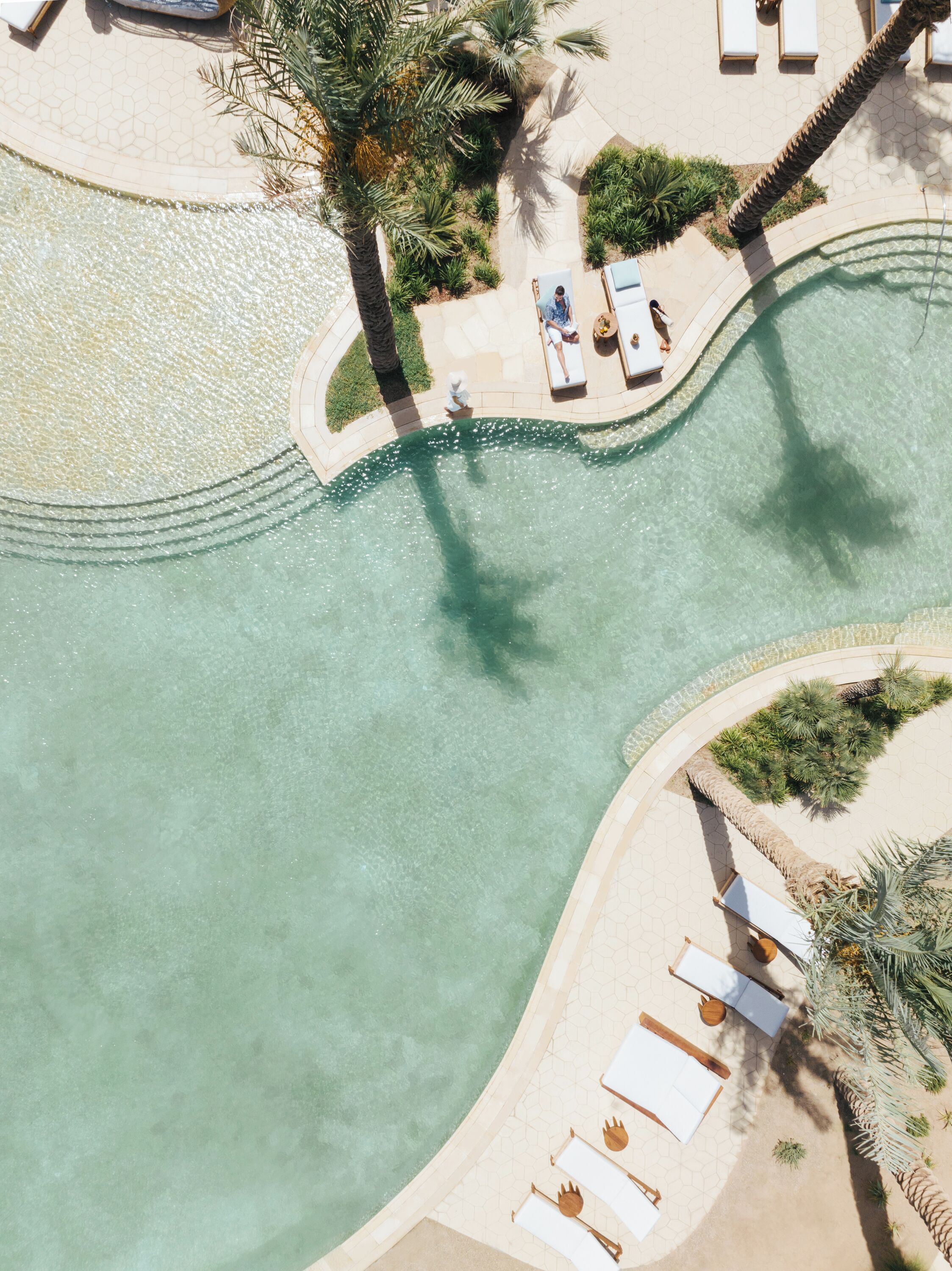 An aerial view of a resort with a swimming pool, lounge chairs, and palm trees.