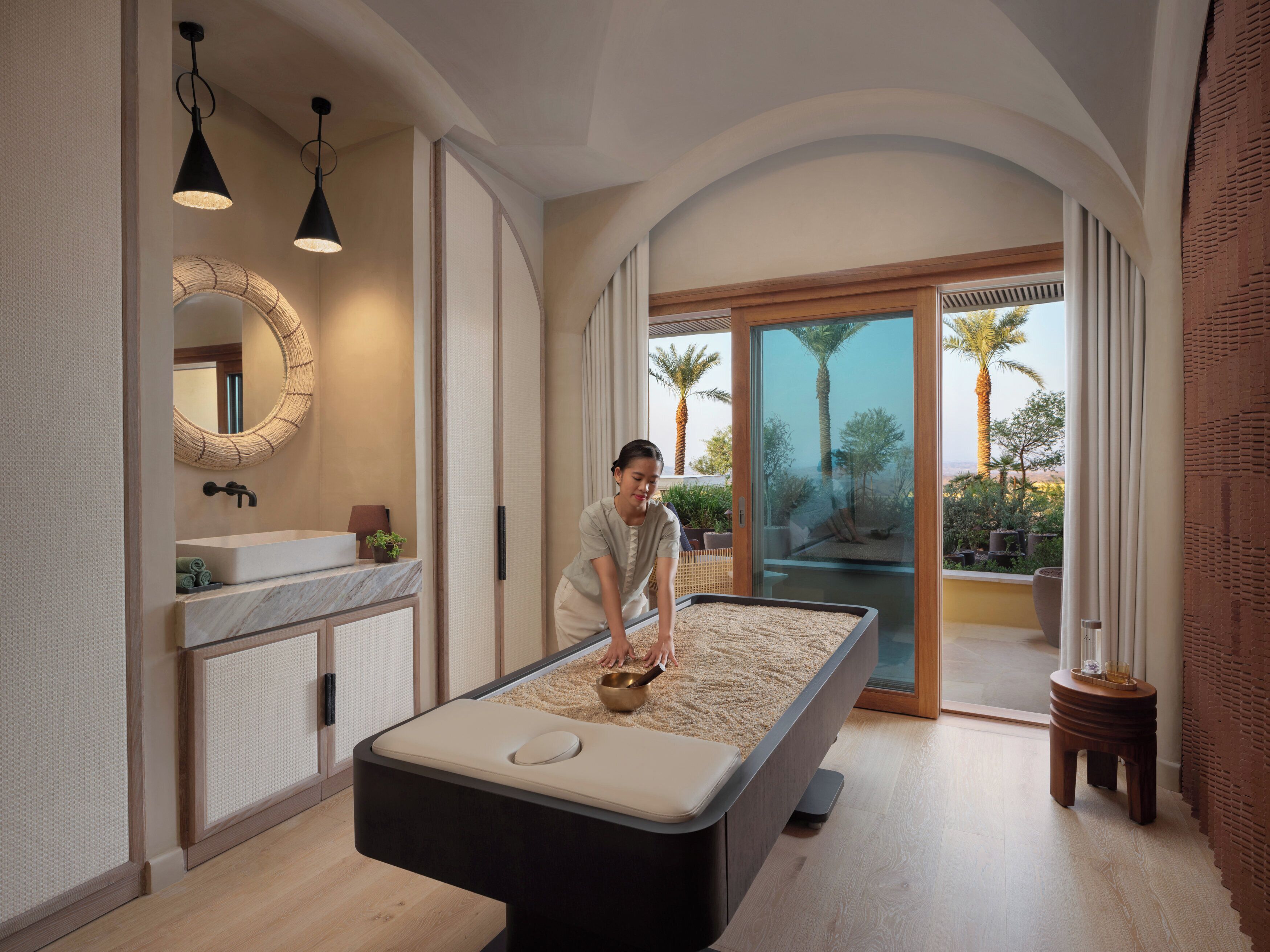 A modern spa room with a massage table, a sink, and a large mirror.