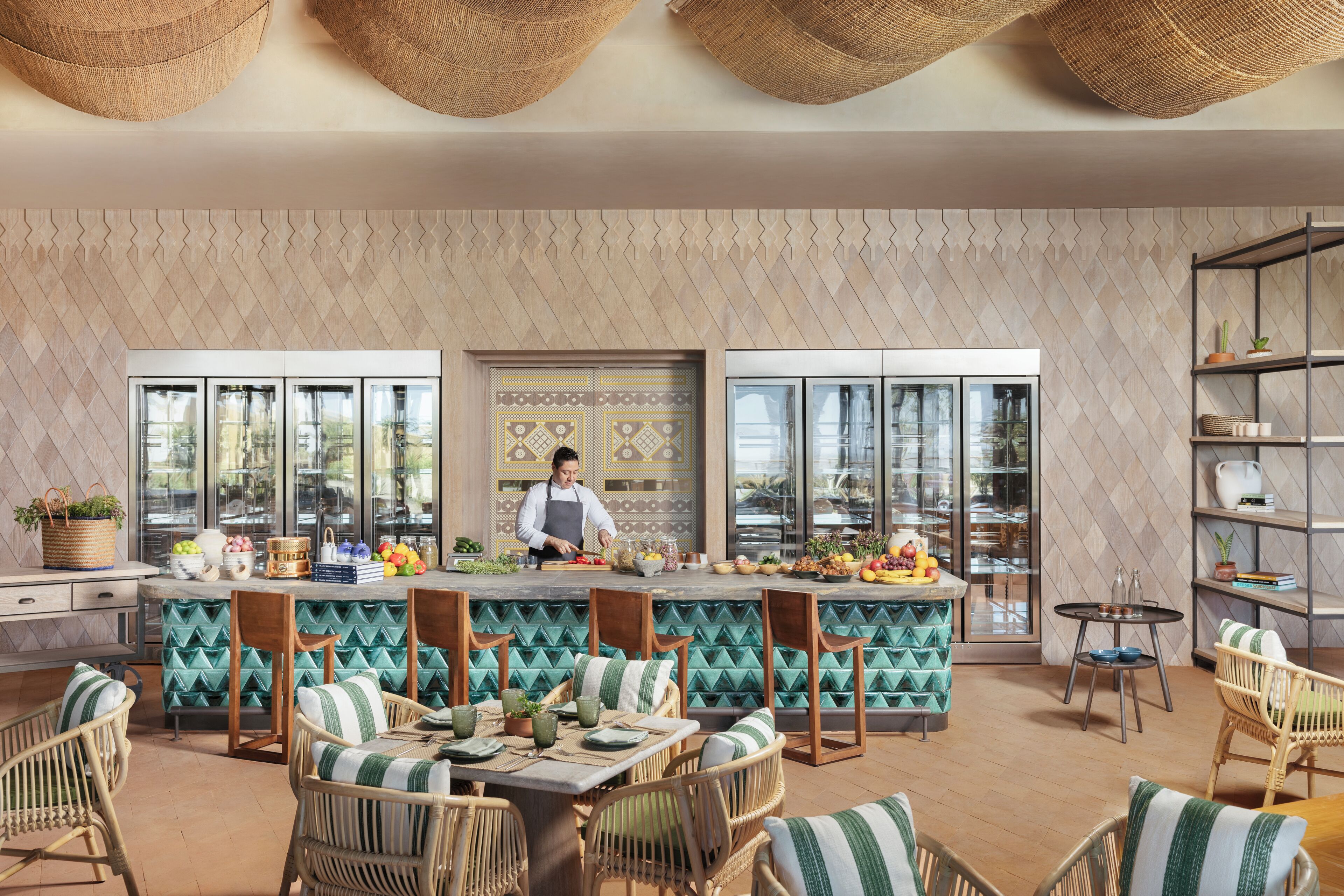 A modern restaurant with a chef preparing food, a bar area, and seating with a patterned wall and large windows.