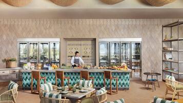 A modern restaurant with a chef preparing food, a bar area, and seating with a patterned wall and large windows.