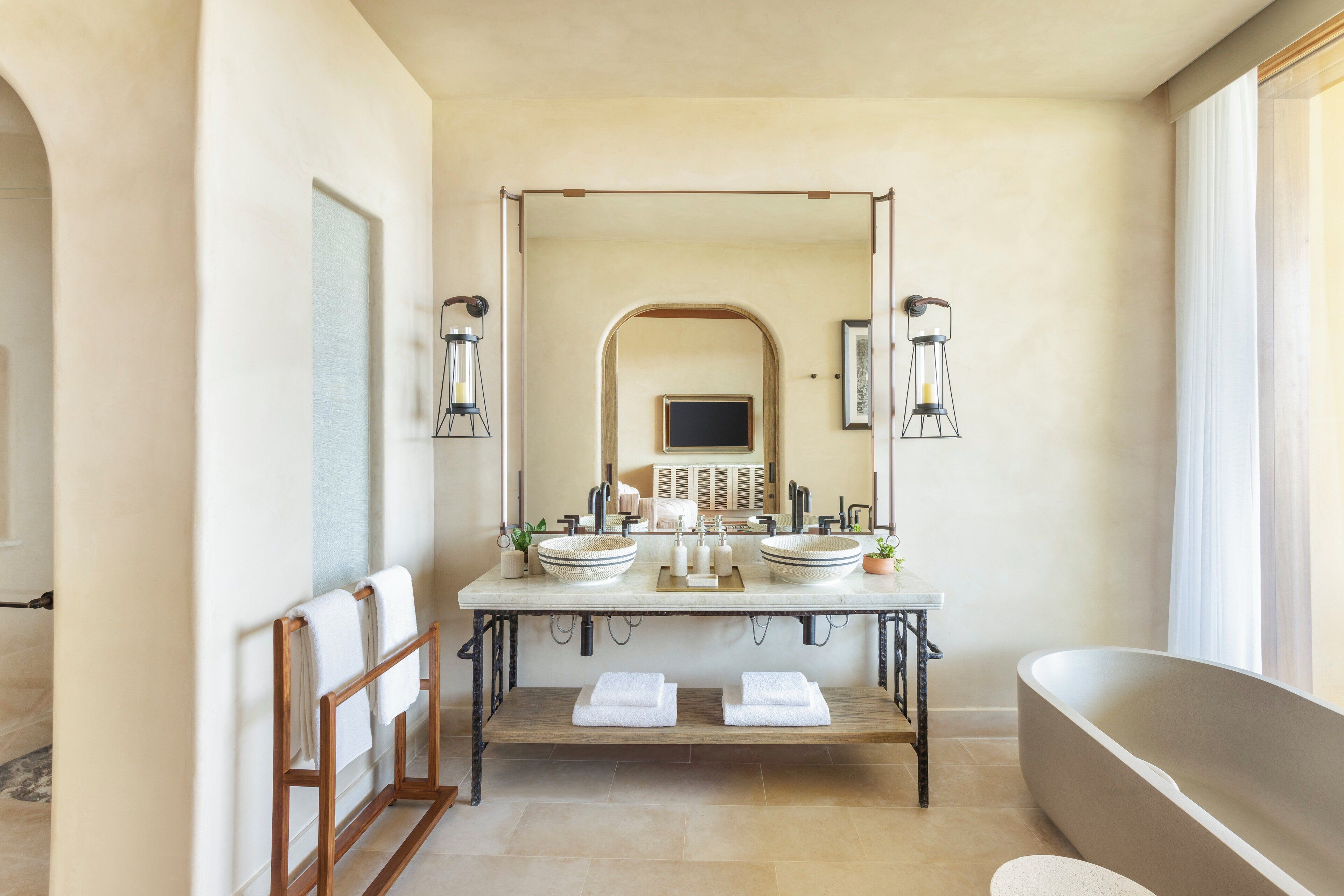 A bathroom with a large bathtub, two sinks, a mirror, and a wooden bench with towels.