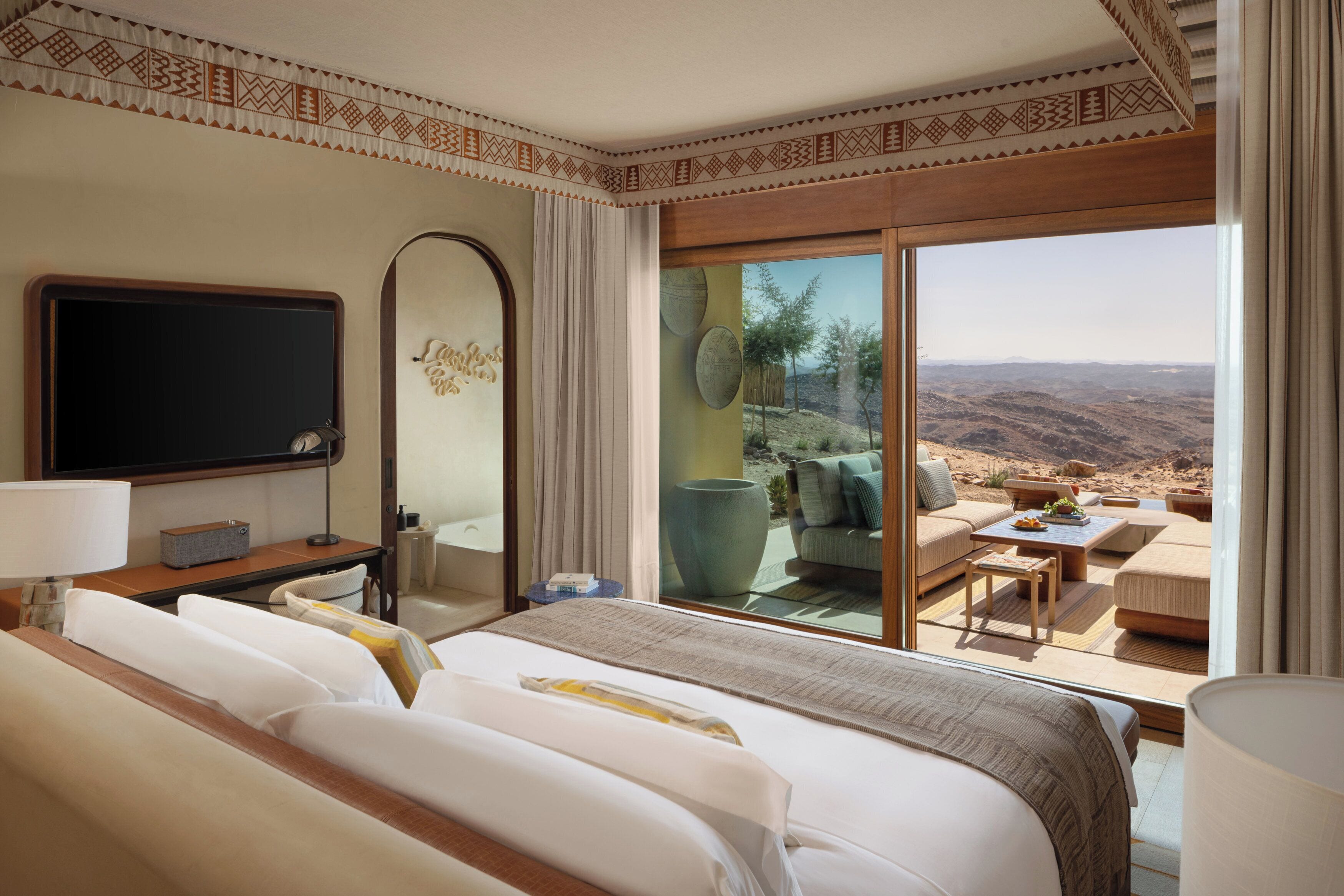 Habitación de hotel con una cama grande, televisión, escritorio y vista a un paisaje desértico a través de una puerta corredera de vidrio.
