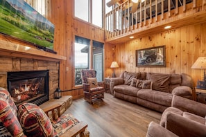 A cozy cabin interior with a fireplace, wooden walls, a sofa, and a television mounted above it.