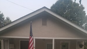 Et etagers hus med en veranda, et amerikansk flag og en lille have med blomster.