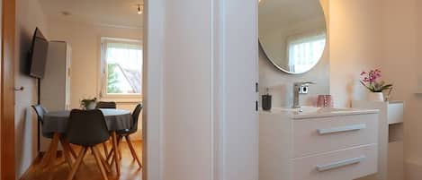 A modern kitchen with a large round mirror, white cabinetry, and a dining area with a table and chairs.