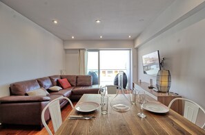Ein modernes Wohnzimmer mit einem braunen Ledersofa, einem Holzesstisch gedeckt mit Tellern, Gläsern und Besteck sowie einem großen Fenster mit Vorhängen.