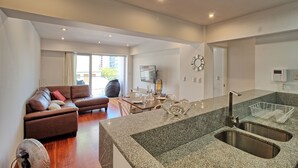 A modern living room with a brown sofa, a dining table, and a kitchen area with granite countertops and a sink. - Beutifull 2 bedroom apartment in the center of Miraflores! Great Location (Miraflores)