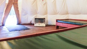 A tent with a wooden floor, a small heater, and a bed with a green mattress. - Sundance Family Tipi (Kananaskis)