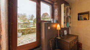 A cozy room with a wooden door leading to a stone courtyard, a small wooden cabinet with a lamp, and a chair. - Tranquil Home in Tinlot (Tinlot)