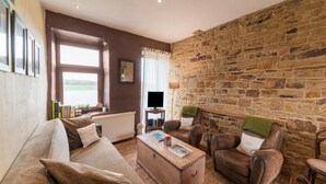 A cozy living room with a stone wall, leather sofas, a wooden coffee table, and a television. - Tranquil Home in Tinlot (Tinlot)