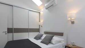 Une chambre d’hôtel moderne équipée d’un lit, d’une table de chevet, d’une chaise, d’un appareil de climatisation et d’un luminaire fixé au mur.