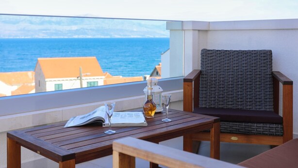 Une table en bois avec une bouteille et des verres, une chaise en osier et une vue sur la mer.