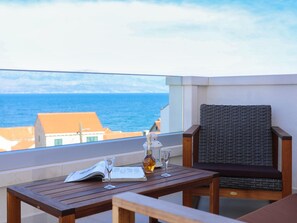 Une table en bois avec une bouteille et des verres, une chaise en osier et une vue sur la mer.