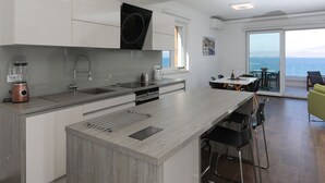 Une cuisine moderne dotée d’un îlot central, un coin repas offrant une vue sur la mer et un balcon avec une table et des chaises.