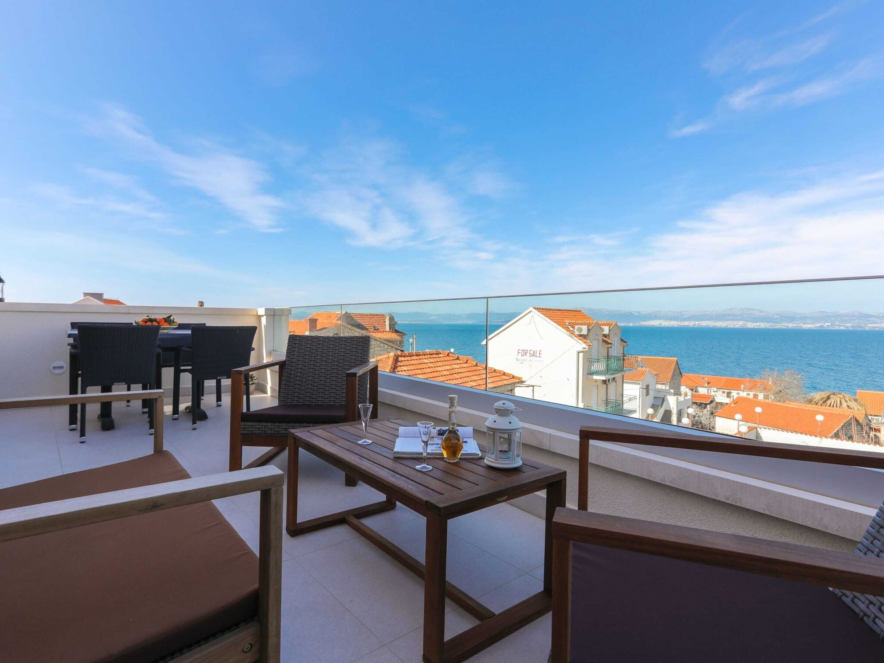 A rooftop terrace with outdoor furniture, a table with drinks, and a view of the sea and buildings.
