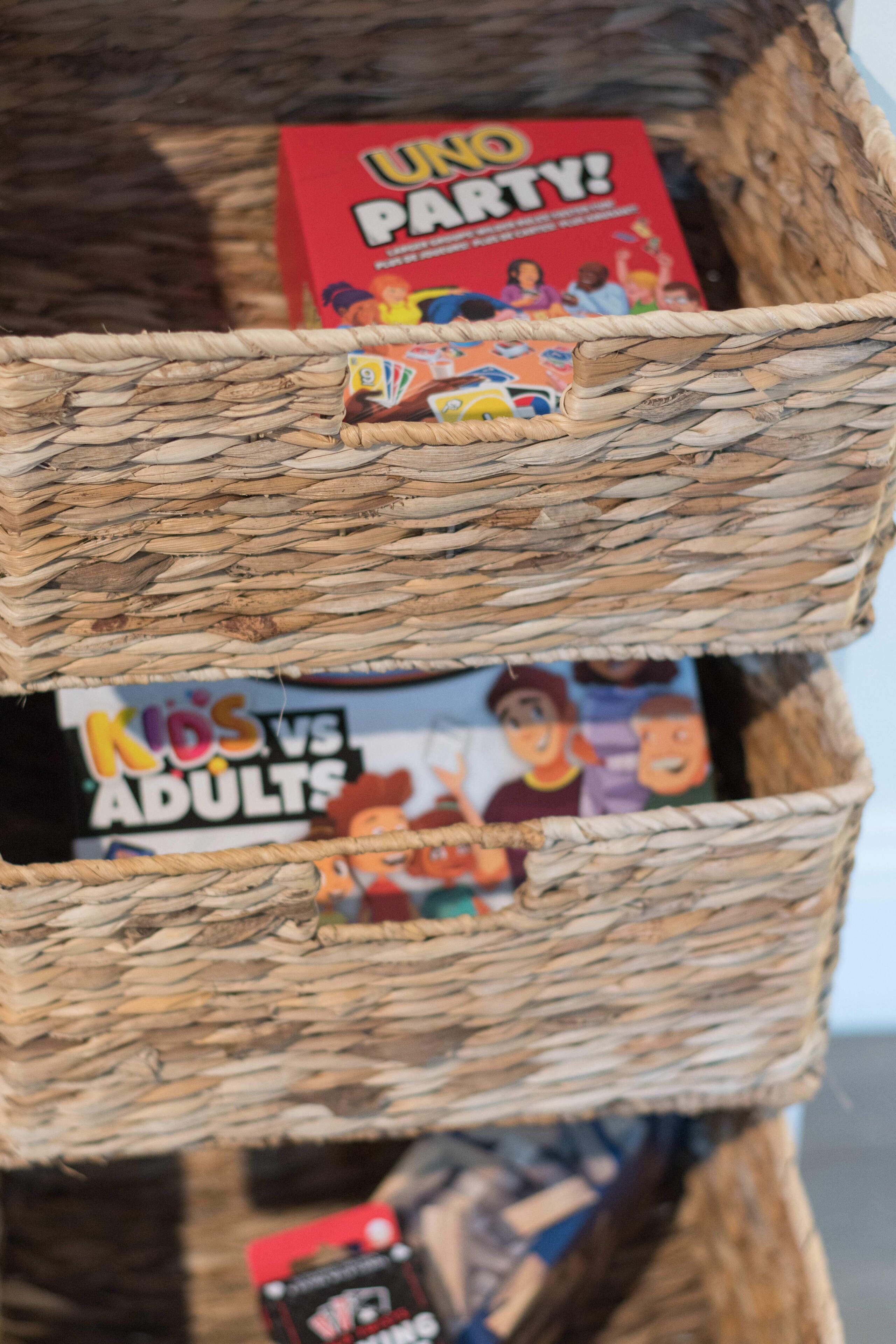 A woven basket containing board games, including UNO PARTY! and KIDS vs ADULTS.