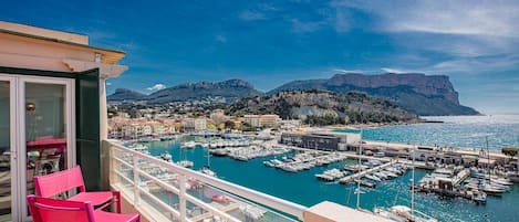 A balcony with pink chairs overlooking a marina with boats and buildings in the background.