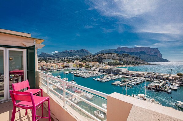 A balcony with pink chairs overlooking a marina with boats and buildings in the background.