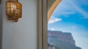 Vista de un paisaje costero a través de una ventana, con un acantilado destacado y una lámpara decorativa de pared.