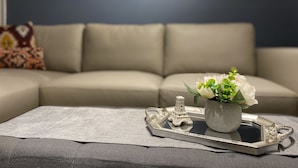 A living room with a beige sofa, a small table with a tray, a vase with white flowers, and a decorative Eiffel Tower. - Walkout 1 Beb, 1 Bath Bsmnt Apt (Ajax)