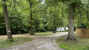 A gravel path leading to a white RV in a wooded area. - Prairie House RV Spaces (Deerfield)