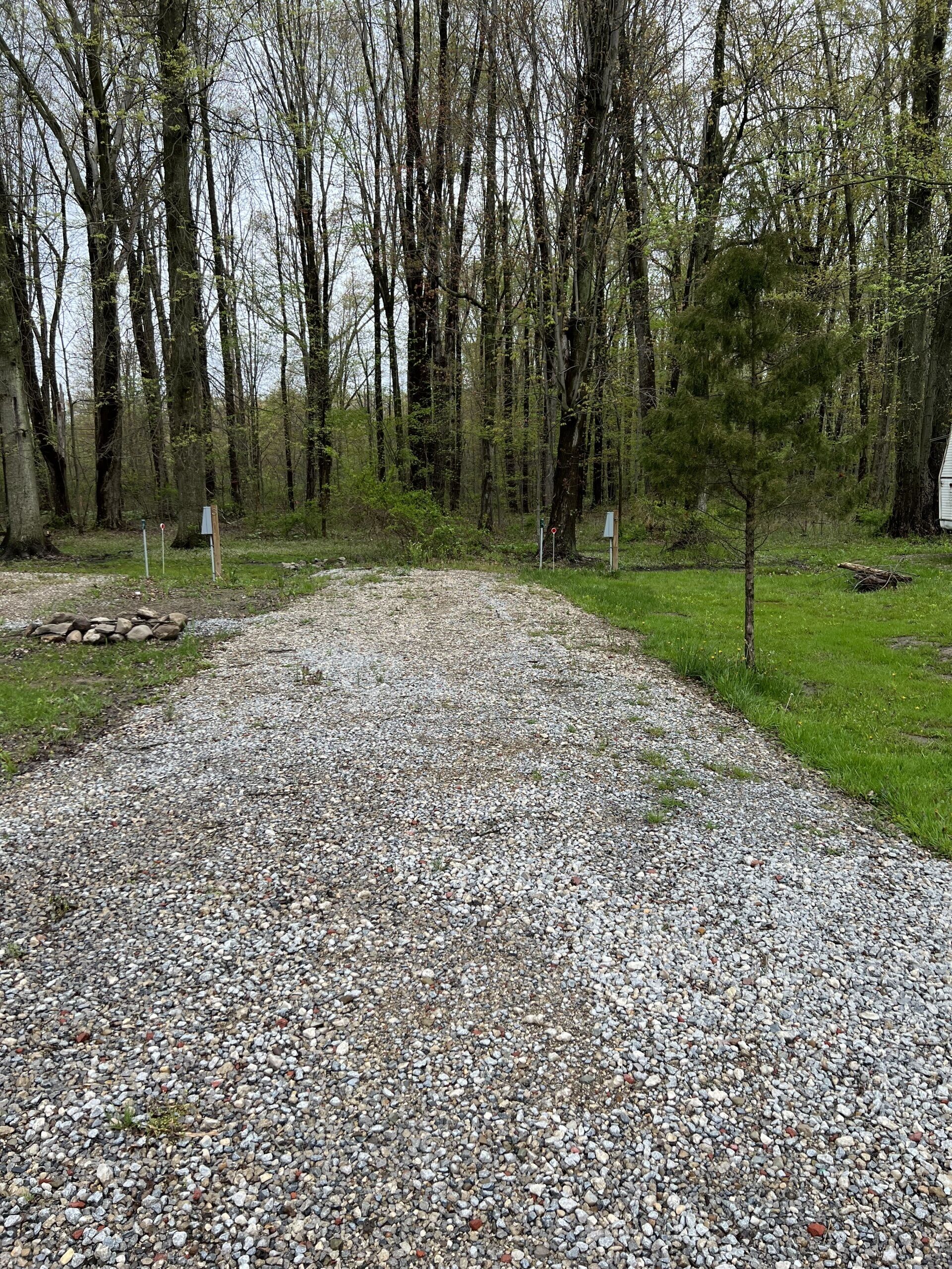 A gravel path leading through a wooded area with trees and a small building in the distance.