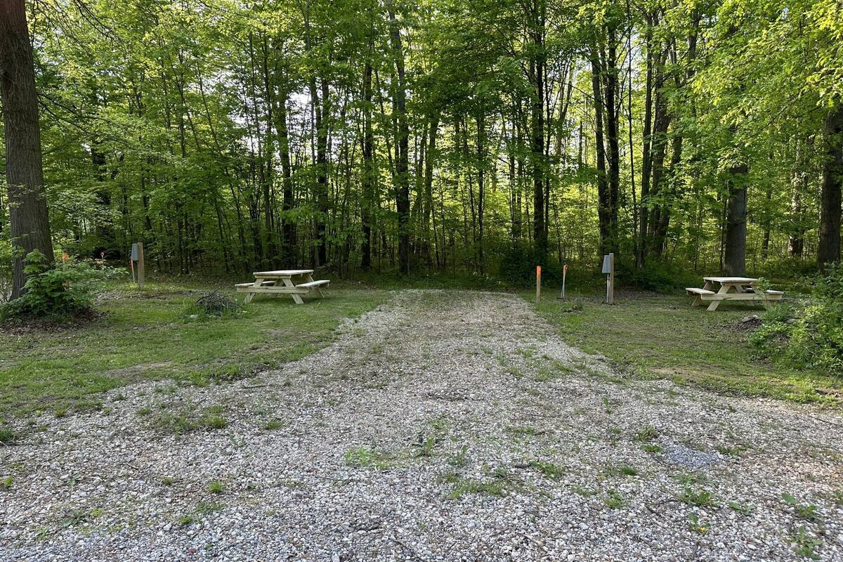 A gravel parking area with picnic tables and a signpost in a wooded setting.