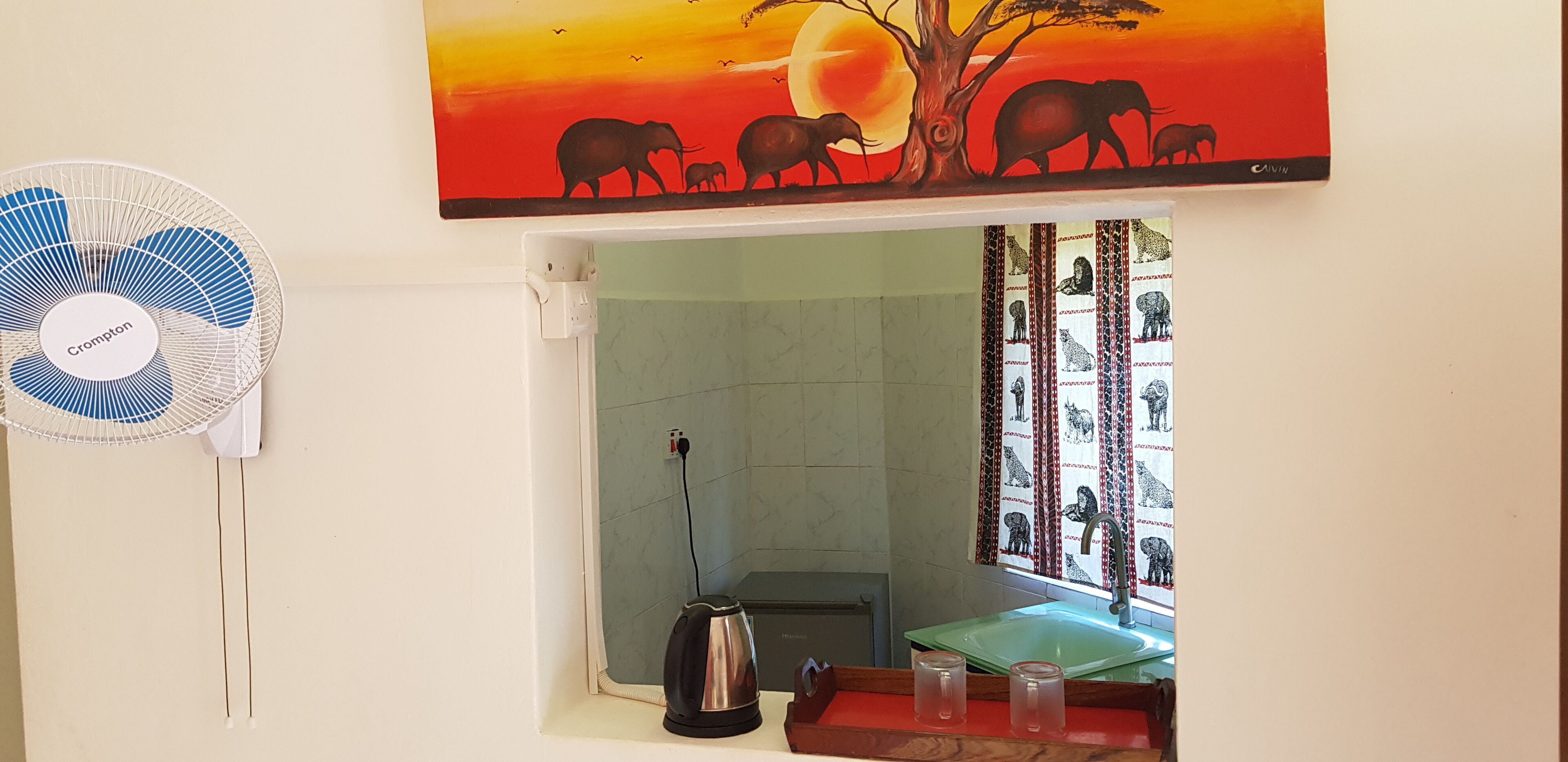 A room with a standing fan, a kettle, and a table with glasses.