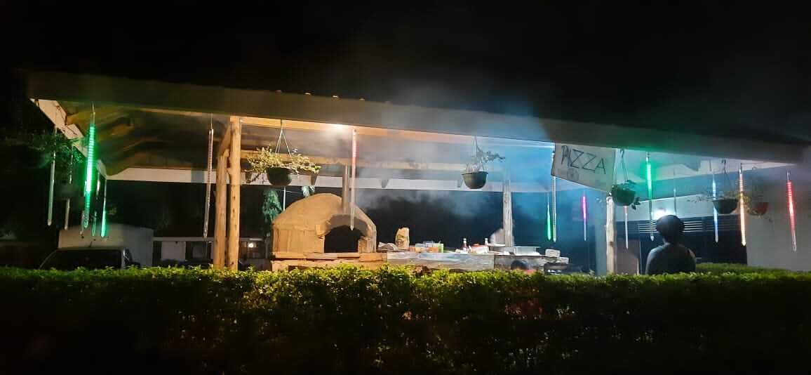 Un restaurant en plein air doté d’un espace dédié à la préparation des pizzas, d’un four à bois et de plantes suspendues.