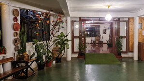 Een hotellobby met een receptiebalie, een groen tapijt en verschillende potplanten.