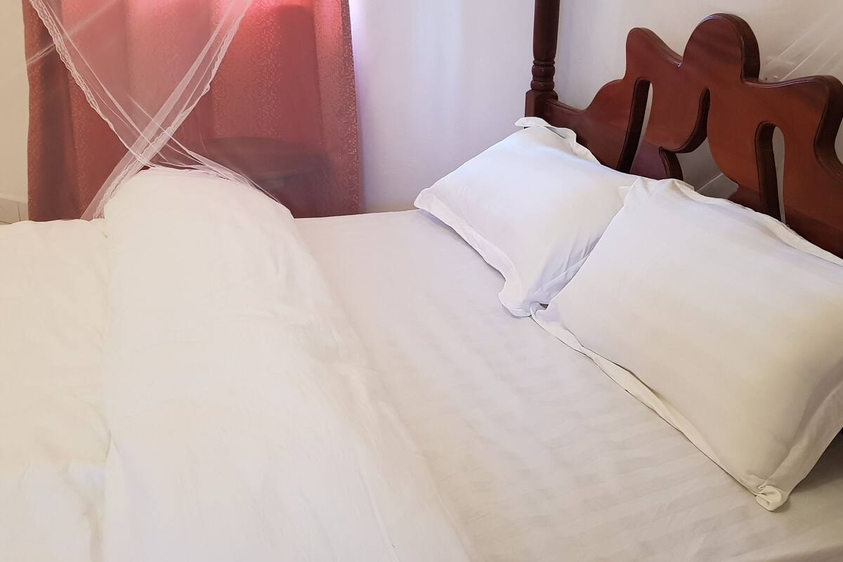 A neatly made bed with white linens and a wooden headboard.