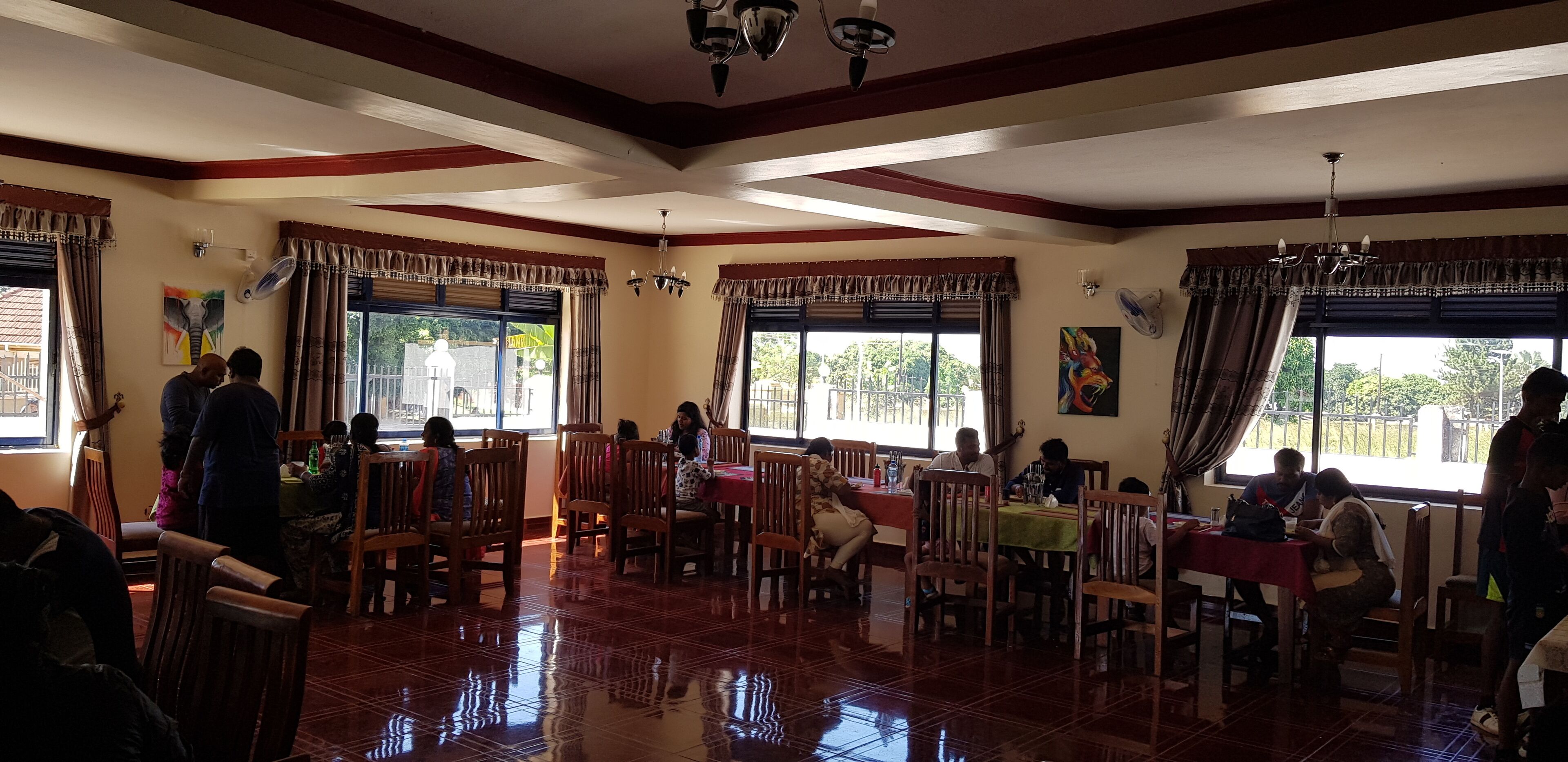 A spacious dining area with multiple tables and chairs, large windows with curtains, and a polished floor.