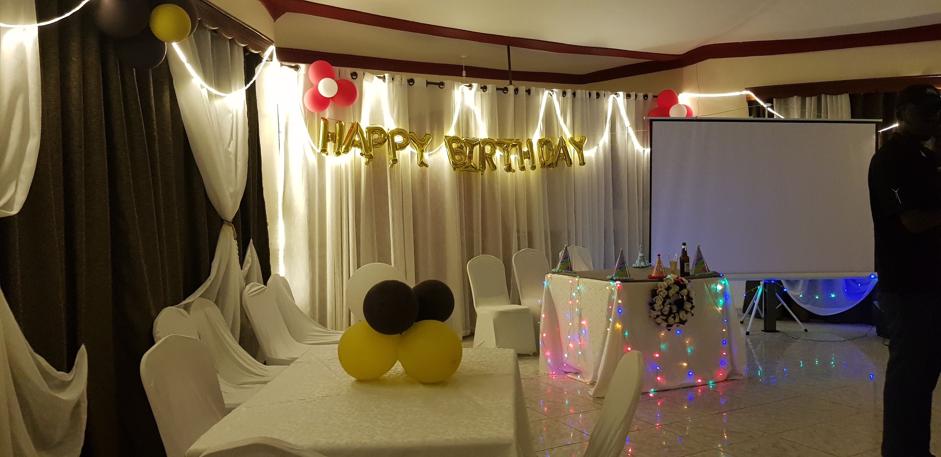 Una habitació amb cortines blanques, una pancarta amb la frase 'Felicitats' i una taula amb estovell blanc i cadires.